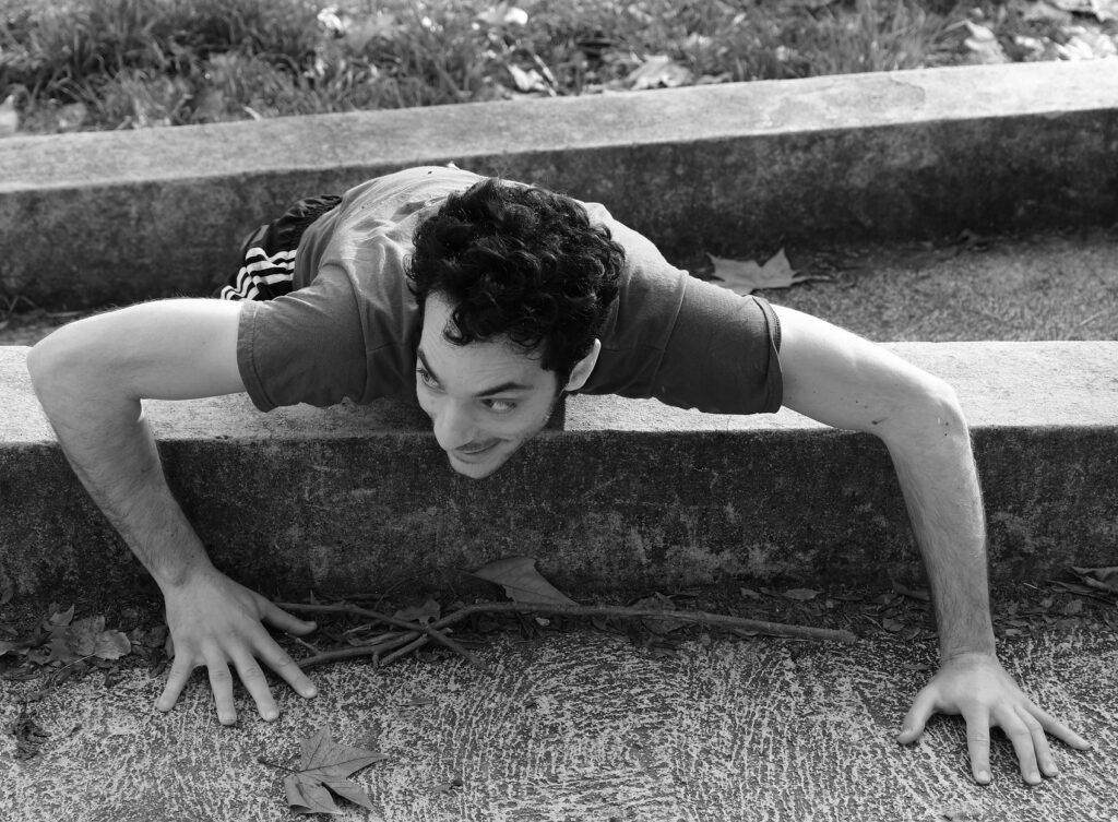 Un homme au sol, vu du dessus, semble observer quelque chose avec un sourire mutin.